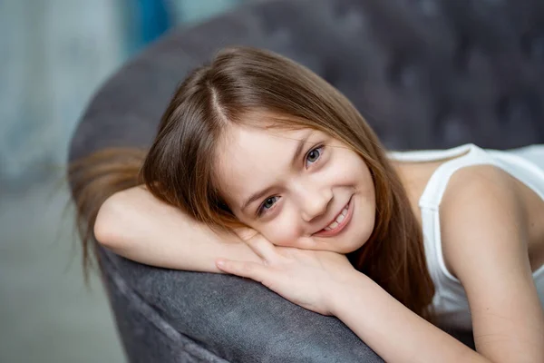Красива дівчина-підліток з довгим волоссям в білому одязі на дивані . — стокове фото
