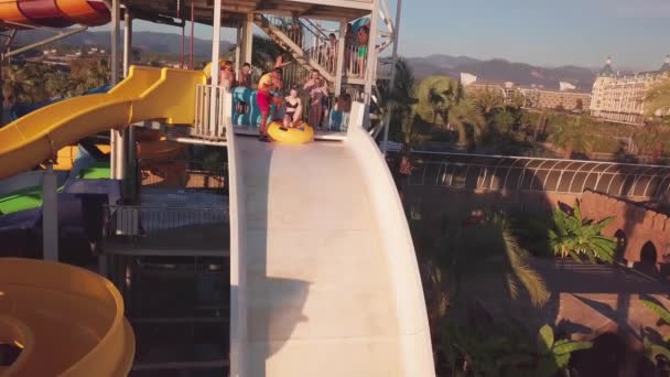 Mädchen sitzt auf einem gelben aufblasbaren Brötchen und rollt die Rutsche im Wasserpark hinunter — Stockvideo
