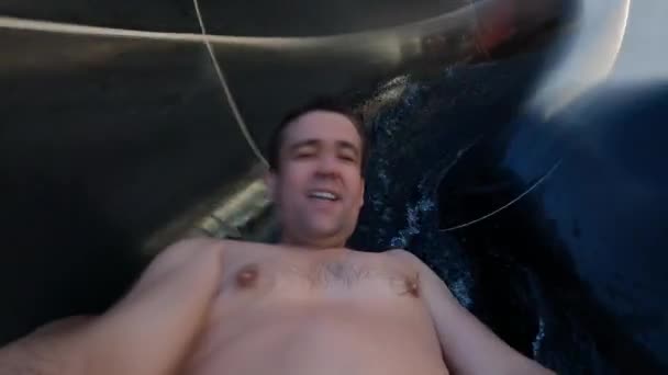 Um homem em uma câmera em suas mãos rola para baixo um slide em um parque aquático. — Vídeo de Stock