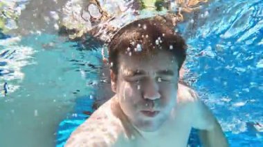 Bir adam elinde kamerayla havuza dalıyor. Suyun altında çekim. 