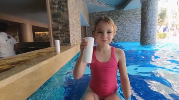 Une petite fille prend un verre assis dans un bar de la piscine. — Video