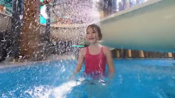 Liten flicka i rosa baddräkt har kul i poolen av vattenrutschbanor med vattenfall. — Stockvideo