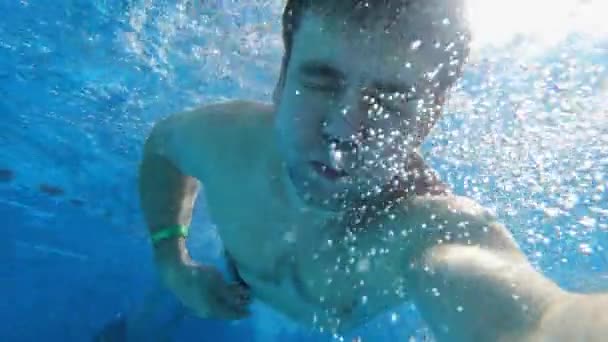 Muž skočí do bazénu s fotoaparátem v ruce. střílení pod vodou. — Stock video