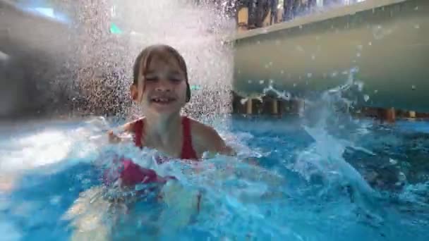 Kleines Mädchen im rosa Badeanzug vergnügt sich im Pool an Wasserrutschen mit Wasserfall. — Stockvideo