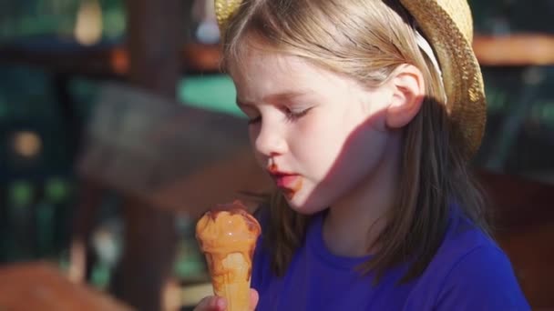 Una niña sucia en un sombrero de paja come un cono con helado. — Vídeo de stock