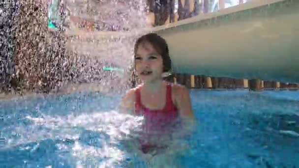 Petite fille en maillot de bain rose s'amuse dans la piscine par des toboggans d'eau avec cascade. — Video