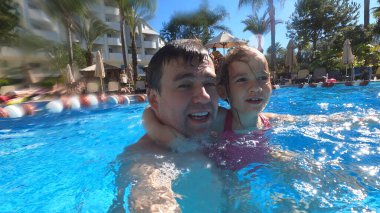 Baba ve kız yüzüyor ve havuzda eğleniyorlar.