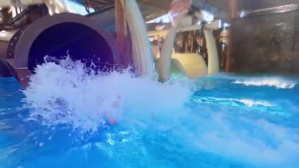 Une petite fille descend la glissière à la piscine dans le parc aquatique. — Video