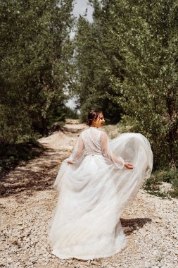 Arkadan bak. Gelinlikli gelin ağaçlar arasında dağ yolunda yürüyor..