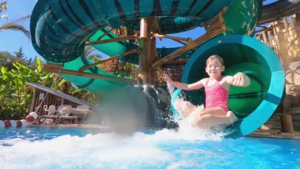 Маленькая девочка скатывается с горки к бассейну в аквапарке. — стоковое видео