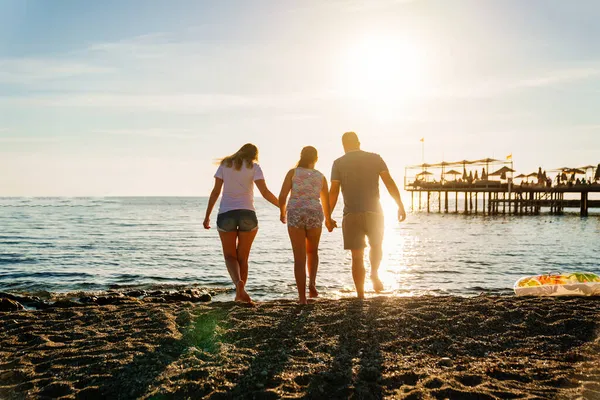 Вид сзади. семья в солнечном свете на берегу морского пляжа. семейный отдых на курорте. — стоковое фото