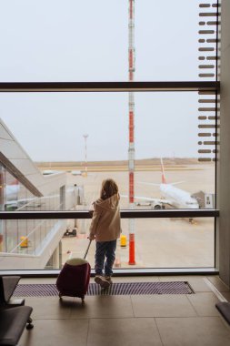 Bavullu küçük bir kız havaalanının penceresinde duruyor.. 