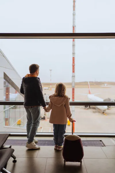 Папа и дочь с чемоданом стоят у окна аэропорта. — стоковое фото