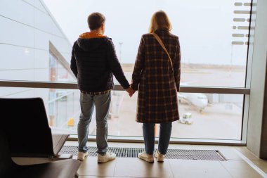 Bir adam ve bir kadın havaalanında pencerede el ele tutuşuyorlar.. 