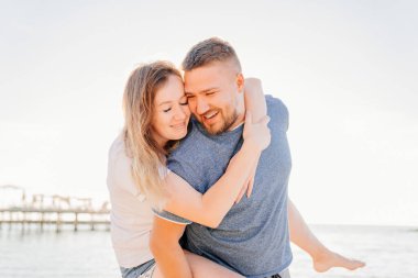 Birbirlerine aşık çiftler sahilde sarılıp eğleniyorlar. Güneş parıltısı