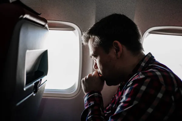 Un hombre con una camisa a cuadros tose en el avión en un asiento de ventana. — Foto de Stock