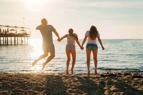 Вид сзади. семья прыгает в солнечном свете на берегу моря. семейный отдых на курорте — стоковое фото