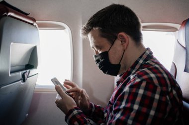 Koruyucu maskeli adam telefondaki mesajda uçaktaki yolcunun koltuğunda..