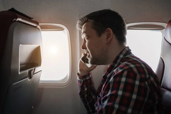 Man i rutig skjorta samtal på telefon i sätet för passagerare ombord på planet. — Stockfoto