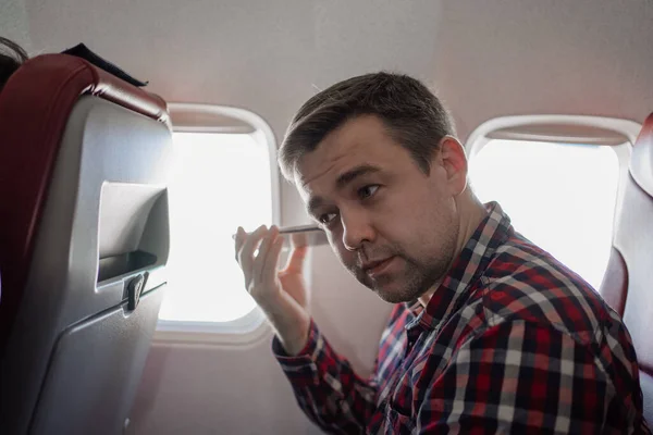 Man i rutig skjorta lyssnar på ett ljudmeddelande på telefon i sittplats ombord på planet — Stockfoto