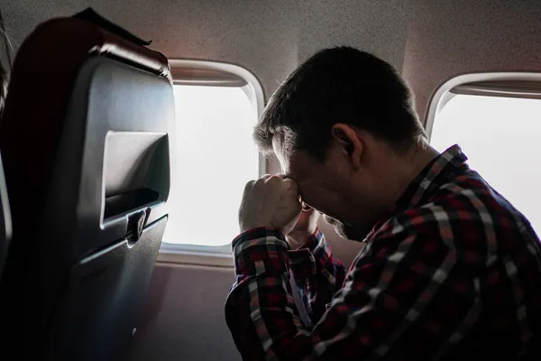 Hombre en camisa a cuadros frota los ojos con las manos en el asiento del pasajero en el avión. — Foto de Stock