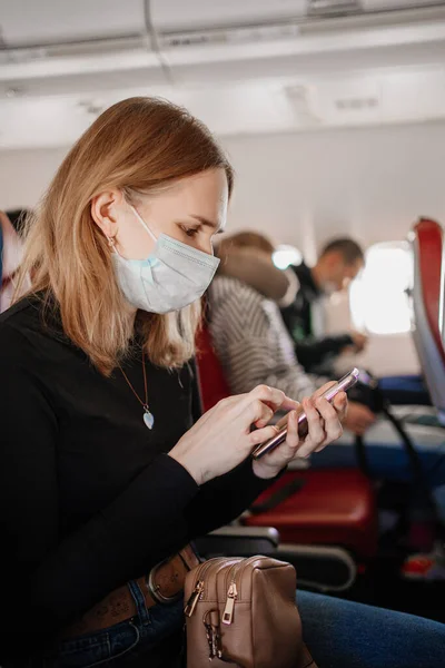 En kvinna bär en skyddande mask skriver sms på telefonen ombord på planet. — Stockfoto