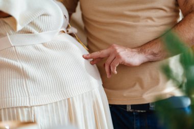 Bir erkek eli, hamile bir kadının karnına parmaklarıyla dokunur.. 