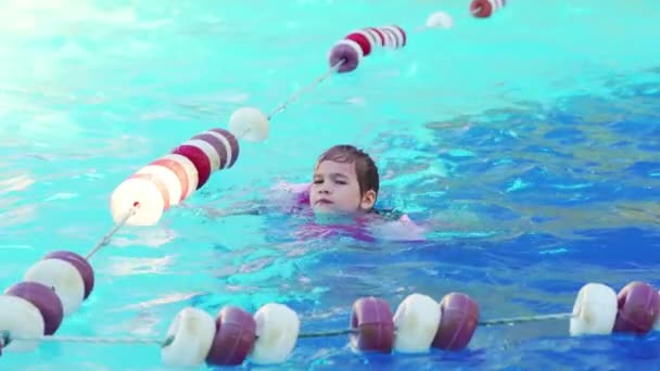 Una niña divertida nada en brazaletes inflables en una piscina cerca de las boyas. — Vídeos de Stock