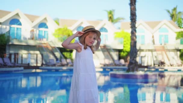Мила маленька дівчинка в білій сукні і солом'яний капелюх біля басейну біля вілли . — стокове відео