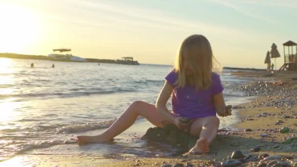 어린 소녀는 바닷가에서 돌을 주워 물 속에 던져 넣는다. — 비디오