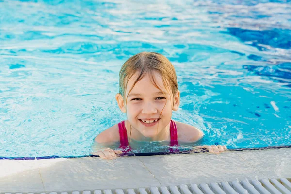 Una niña divertida aprende a nadar sin ayuda al lado de la piscina. — Foto de Stock