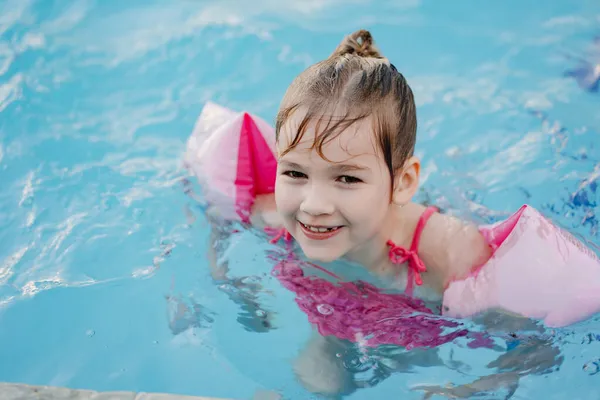 Una niña divertida nada y juega en brazaletes inflables en una piscina — Foto de Stock