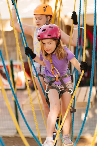 Dos niñas valientes en un casco, camiseta y pantalones cortos sube en un parque de cuerdas — Foto de Stock