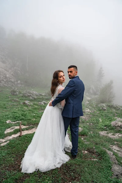 Yeni evliler sisli dağ ormanlarında sarılıyorlar. Yolculukta düğün — Stok fotoğraf