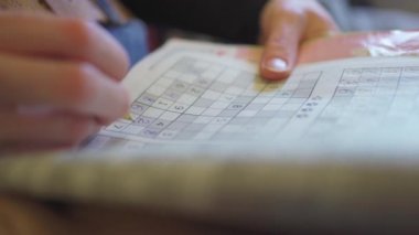 Seçici odaklanma. Kalemli kadın eli matematik bulmacasına rakamlar yazar.