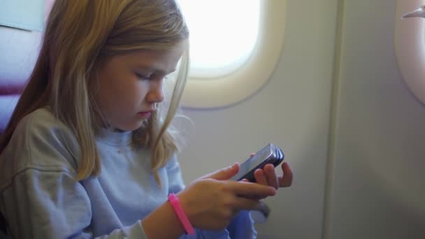 Una niña juega su teléfono mientras vuela en un avión. — Vídeo de stock