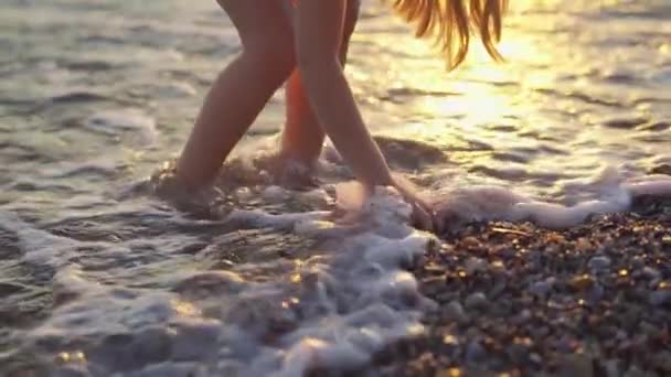 Al atardecer la niña camina a lo largo de la orilla del mar y arroja piedras al agua. — Vídeo de stock