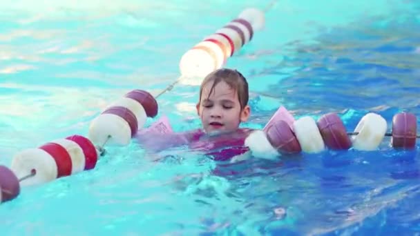 Une drôle de petite fille nage dans des brassards gonflables dans une piscine près des bouées. — Video