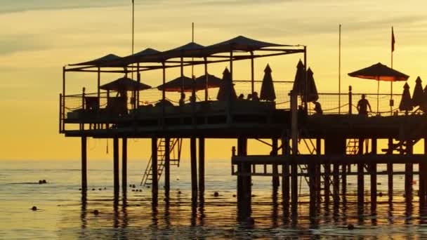 Brygga med parasoller och solstolar. silhuetter. vacker solnedgång på havet. — Stockvideo