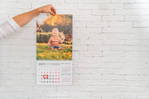 Mens mão mantém calendário com foto de criança na frente de. produtos impressos — Fotografia de Stock