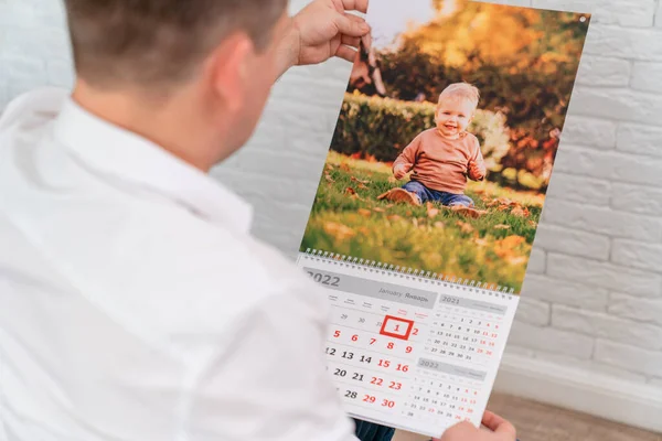 L'uomo tiene un calendario con una foto di un bambino. prodotti stampati. — Foto Stock