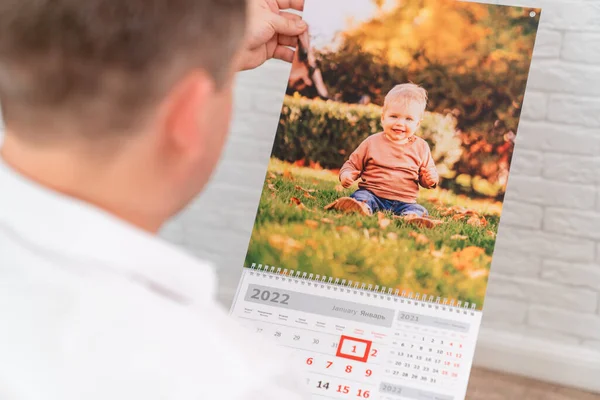 Homem detém um calendário com uma foto de uma criança. produtos impressos. — Fotografia de Stock