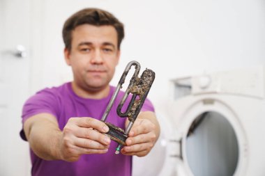 Çamaşır makinesinin tamircisi eski boru elektrikli ısıtıcıyı tutuyor. 