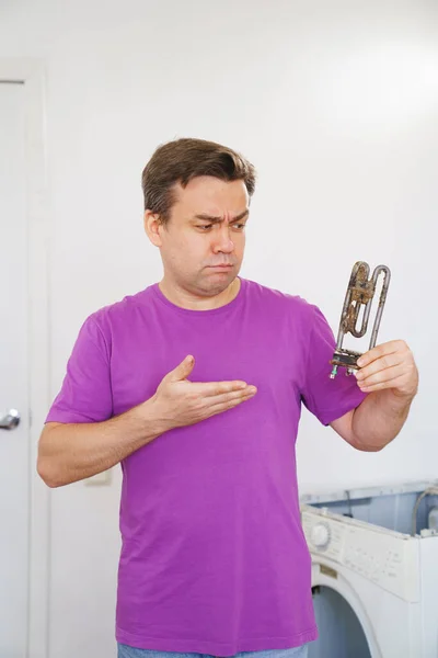 Triste reparador de lavadora sostiene viejo calentador eléctrico tubular — Foto de Stock