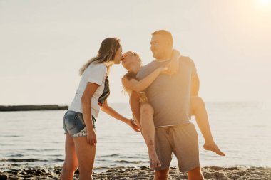 Mutlu bir aile. Anne kızını öpüyor. Baba kızını deniz kıyısına götürüyor.. 