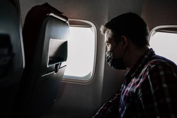 Ein Mann mit schwarzer Schutzmaske und kariertem Hemd am Fenster des Flugzeugs. — Stockfoto
