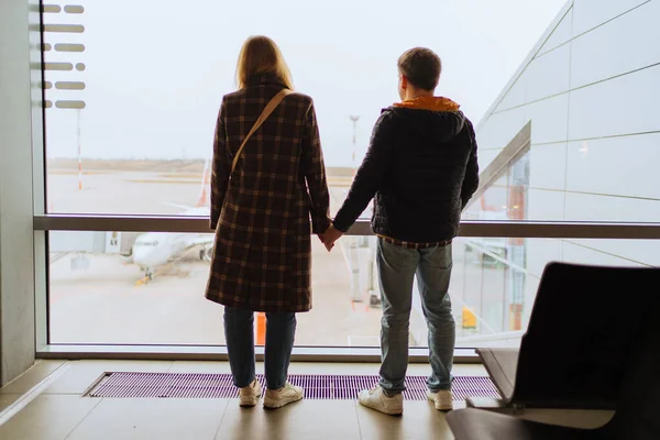 Um homem e uma mulher de mãos dadas junto à janela do aeroporto. — Fotografia de Stock