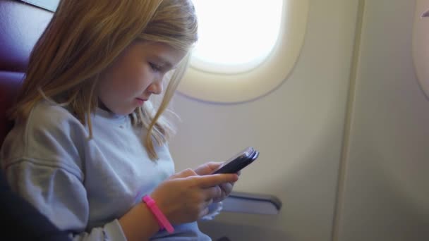 Маленькая девочка играет в телефон во время полета в самолете. — стоковое видео