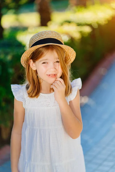 Niña con un vestido blanco y un sombrero de paja en el camino en un hotel tropical —  Fotos de Stock