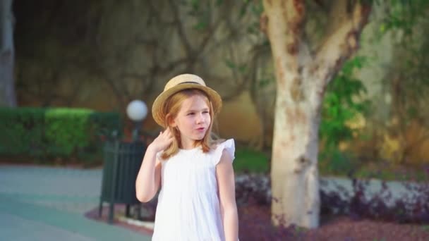 Веселая девушка в белом платье и соломенной шляпе весело прогуливается по тропинке — стоковое видео